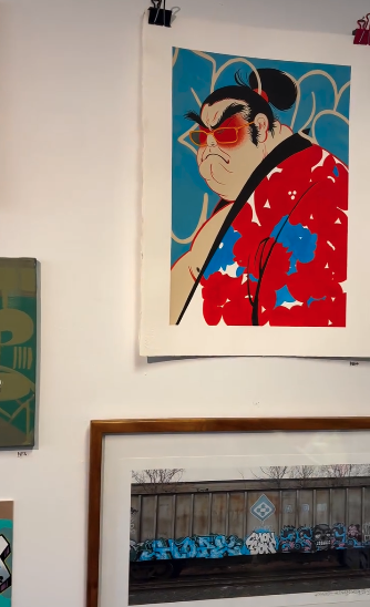 Street-inspired forms and emotion: echoes of BHIVER’s legacy Portrait painting of a man in red, displayed above framed street art